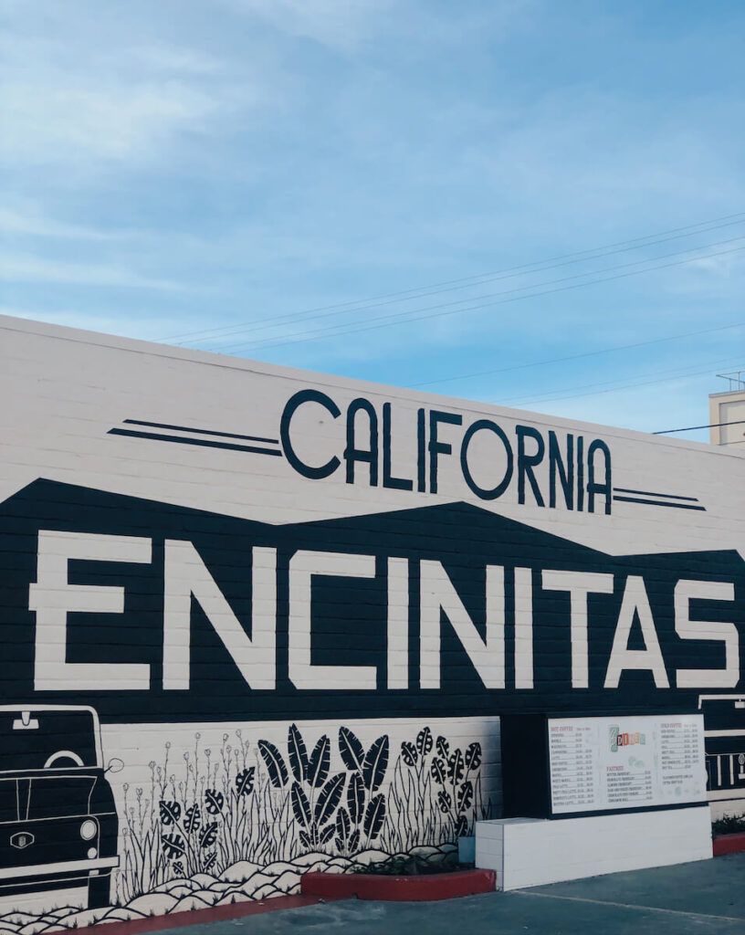 A black and white mural on a brick wall in Encinitas. It says California Encinitas, and features some plants and a vintage looking car.