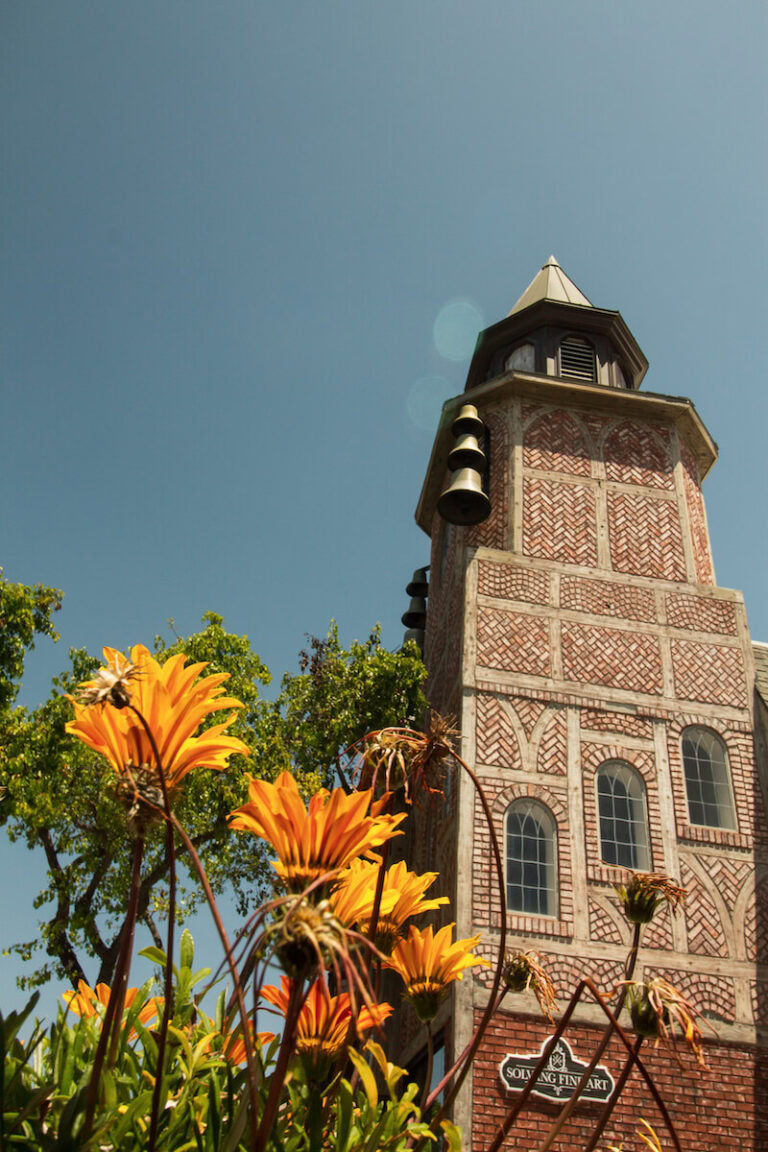 A large brick tower with bells on the side, and orange flowers in front of it