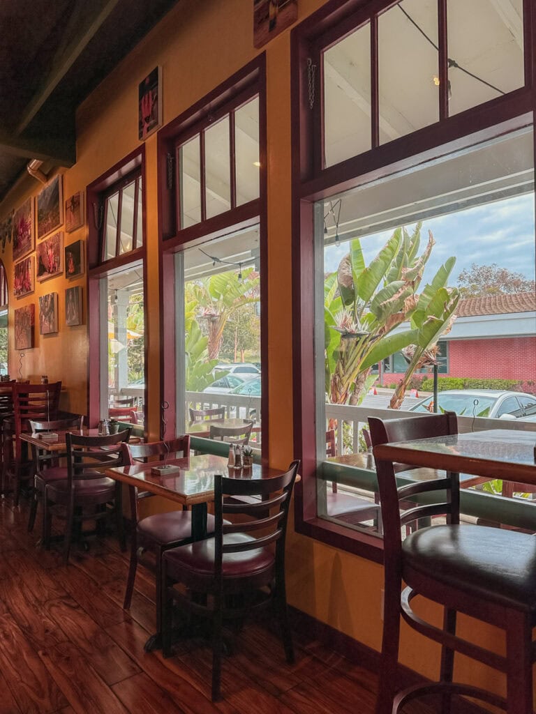 The interior of Lotus Cafe in Encinitas. There are dark wood tables and chairs in front of large windows.