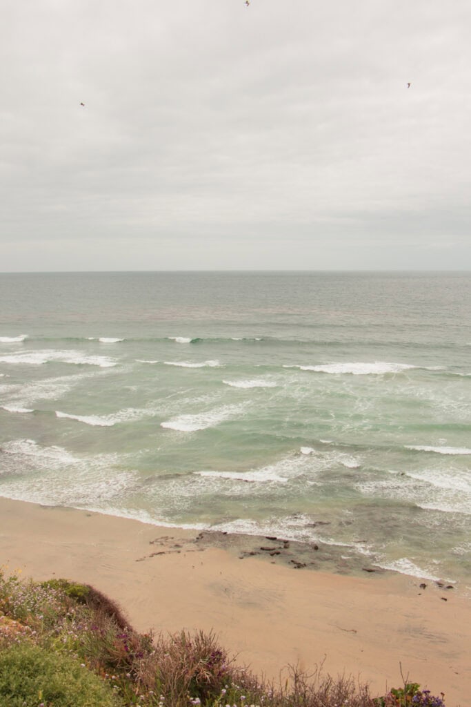 Moonlight Beach on a cloudy day. There are choppy waves coming onto the shores. 