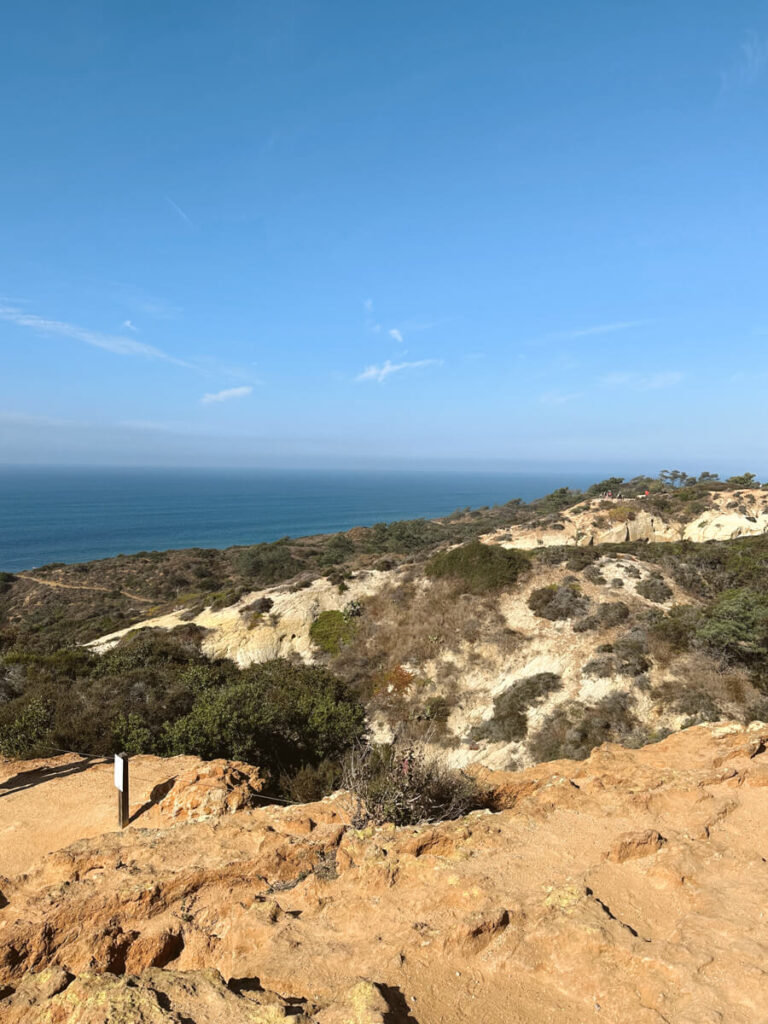 View from the top of the coastal cliffs. You can see the ocean in the distance and the sandy and rocky coastal cliffs in the foreground on a sunny day at Torrey Pines State Reserve.