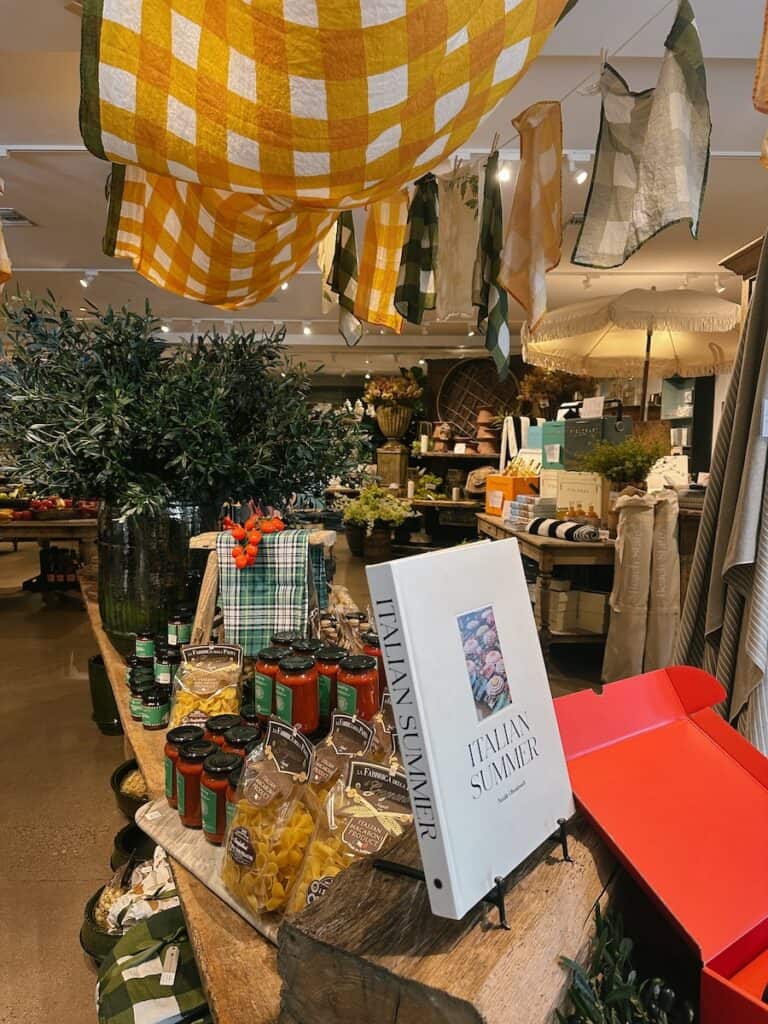 The interior of Field and Fort in Summerland. There is a table with books and jars of sauces, and a yellow and white checkered cloth hanging from the ceiling.