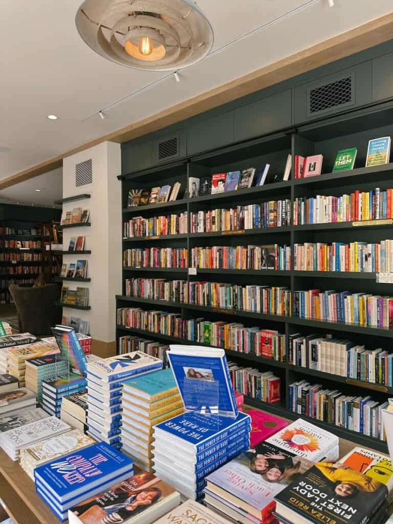 The interior of Godmothers Bookstore. There is a dark green blue bookshelf, and another table in front of it with more books.