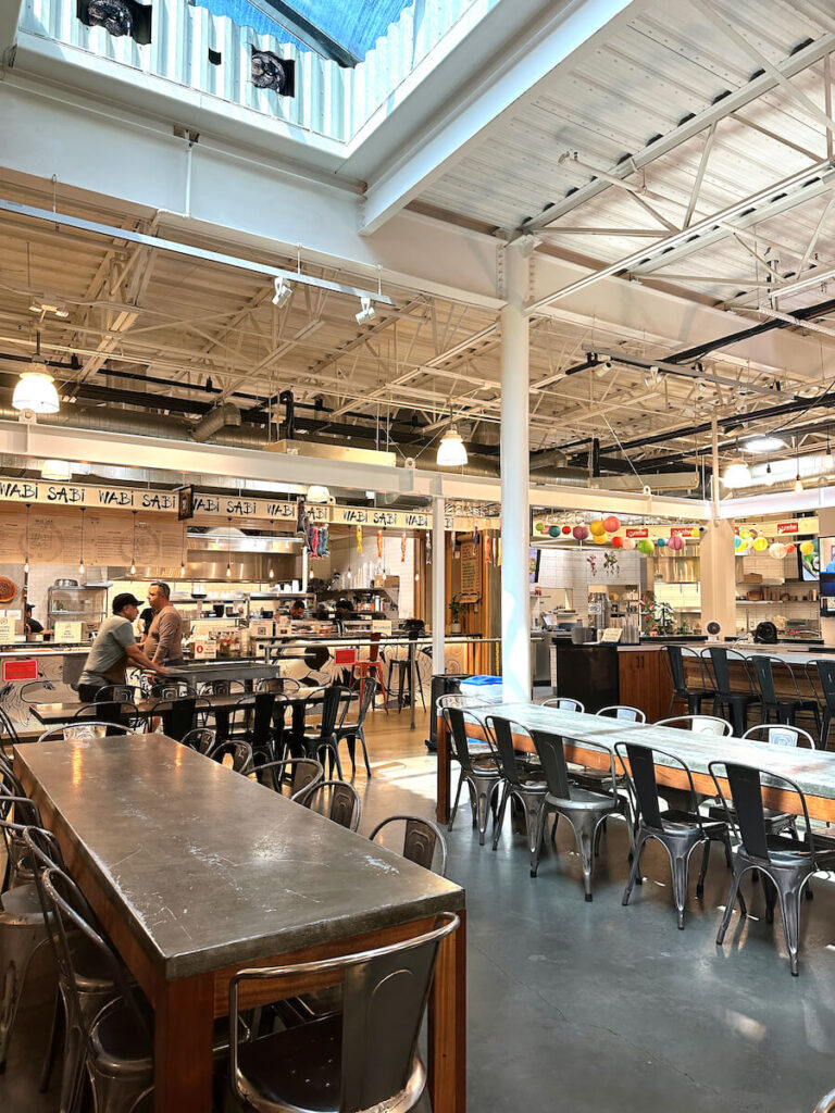 Interior of the Santa Barbara Public Market. There are long tables and food stands on the perimeter.