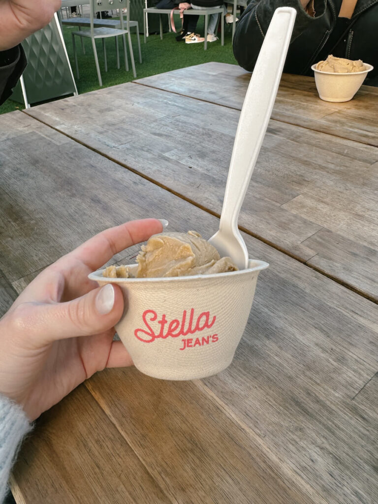 A single scoop of coffee ice cream in a cup that reads "Stella Jean's" on the front in pink. 