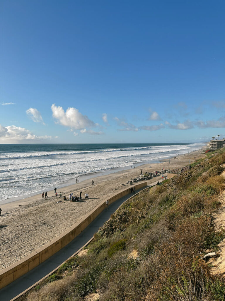 View looking down at Carlsbad State Beach. There is a biking path next to the sand.