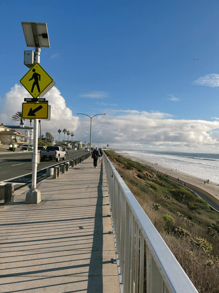 A sidewalk along Carlsbad Boulevard, with the view of Carlsbad State Beach below on the right.