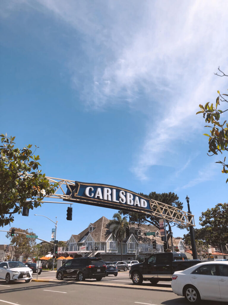 A blue and white sign that says "Carlsbad" over a busy intersection in town.