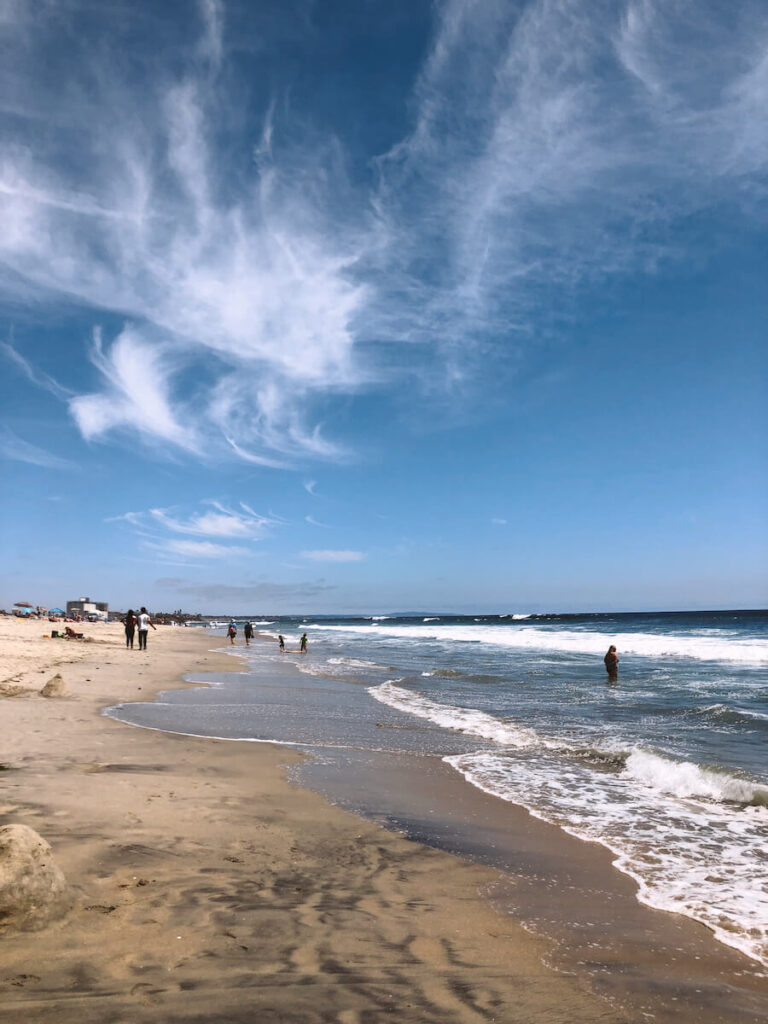 A few beachgoers sitting on the beach and wading in the water at a beach in Carlsbad.