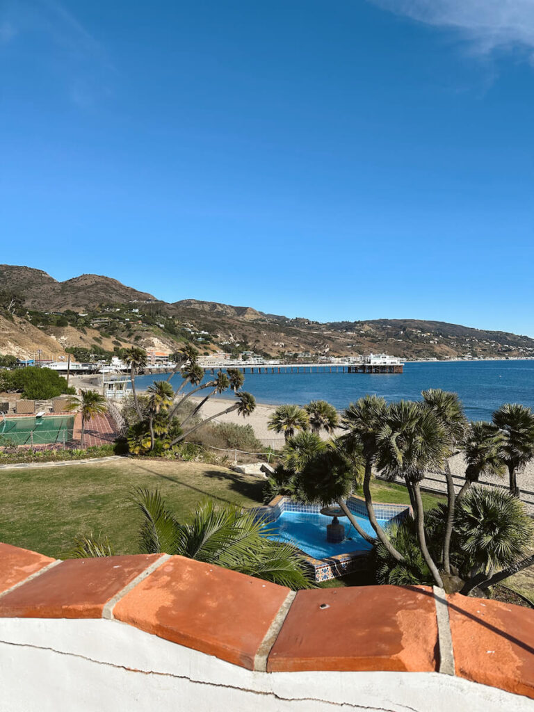 The view from the balcony at Adamson House. The lawn with a star-shaped fountain is in the foreground, and in the background you can see the ocean, the Malibu Pier, and the Santa Monica Mountains