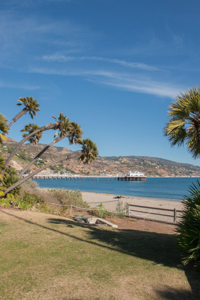 View from the Adamson House lawn, looking out to the ocean and the Malibu Pier. There are palm trees on either side of the image,