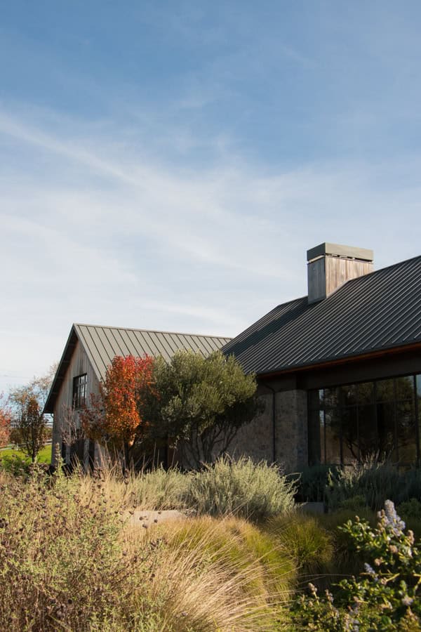 The exterior of Brave and Maiden Vineyards in Solvang, CA. There is a modern stone building, and a variety of plants growing in front of it.