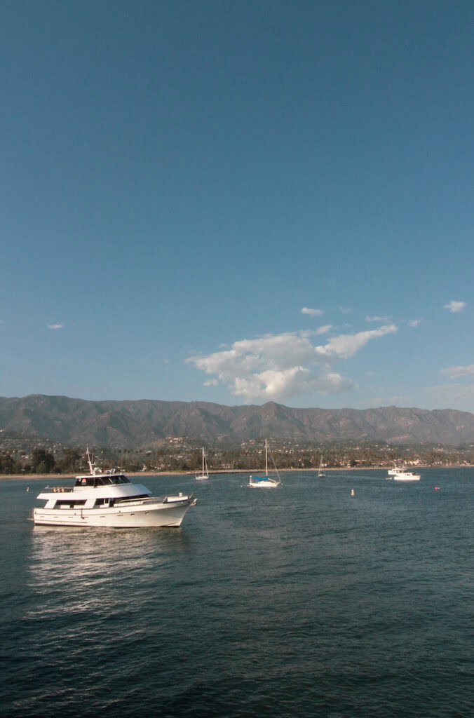 View from Stearns Wharf in Santa Barbara. White boats sitting in the water, with the coastline and mountains in the background