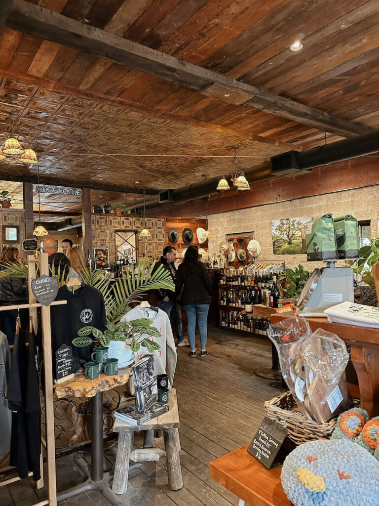 The inside of Cornell Wine Co. There is a shelf of wine bottles in the background, and in the foreground, there are tables with other goods being sold.