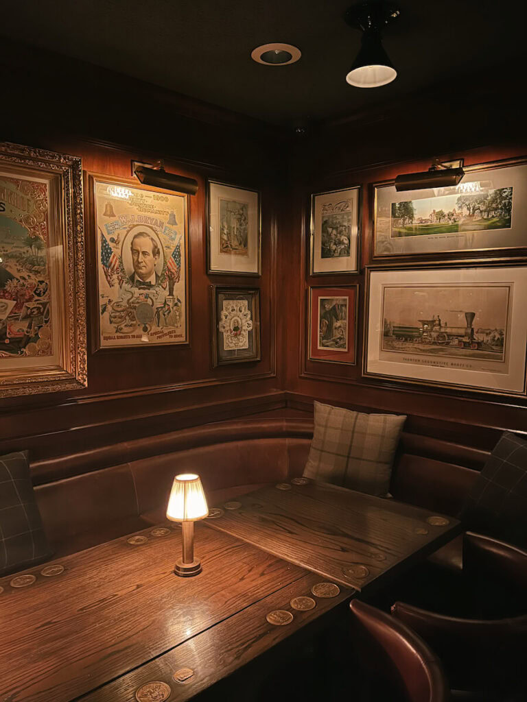 An empty booth at Bud's with a dim lamp on the table an an eclectic mix of historic pieces hung up on the wall.