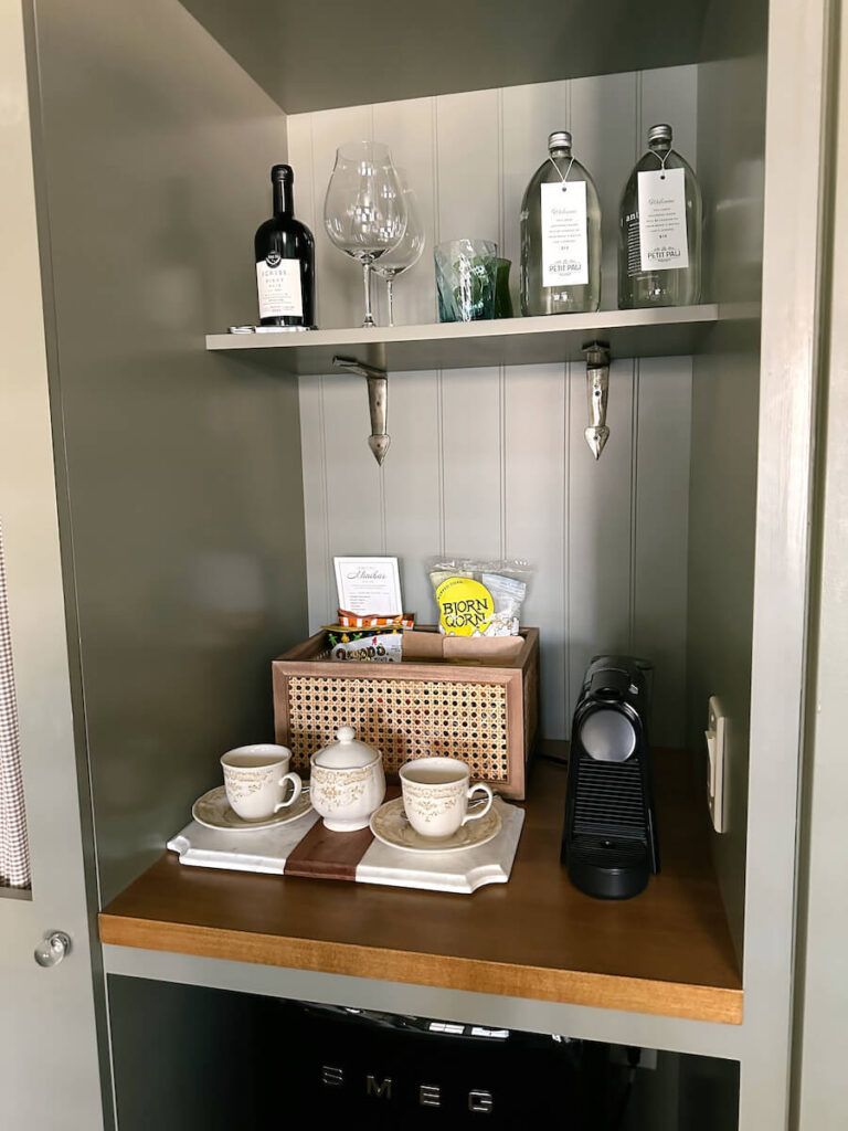 An espresso machine and two tea cups, a basket of snacks, and glasses and a bottle of wine in a room at Le Petit Pali