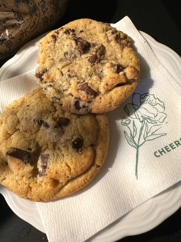 Two chocolate chip cookies on top of a napkin that says "Cheers"