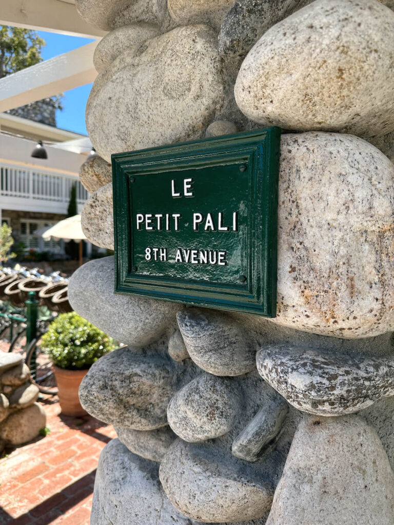 A green sign hung on a stone wall. The sign reads "Le Petit Pali 8th Avenue"