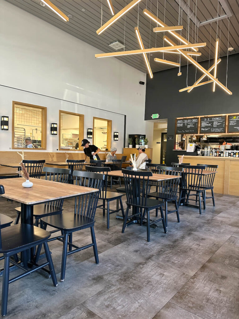 The modern interior of Rise and Roam. There are wood tables with black chairs, and a cash register in the background. 