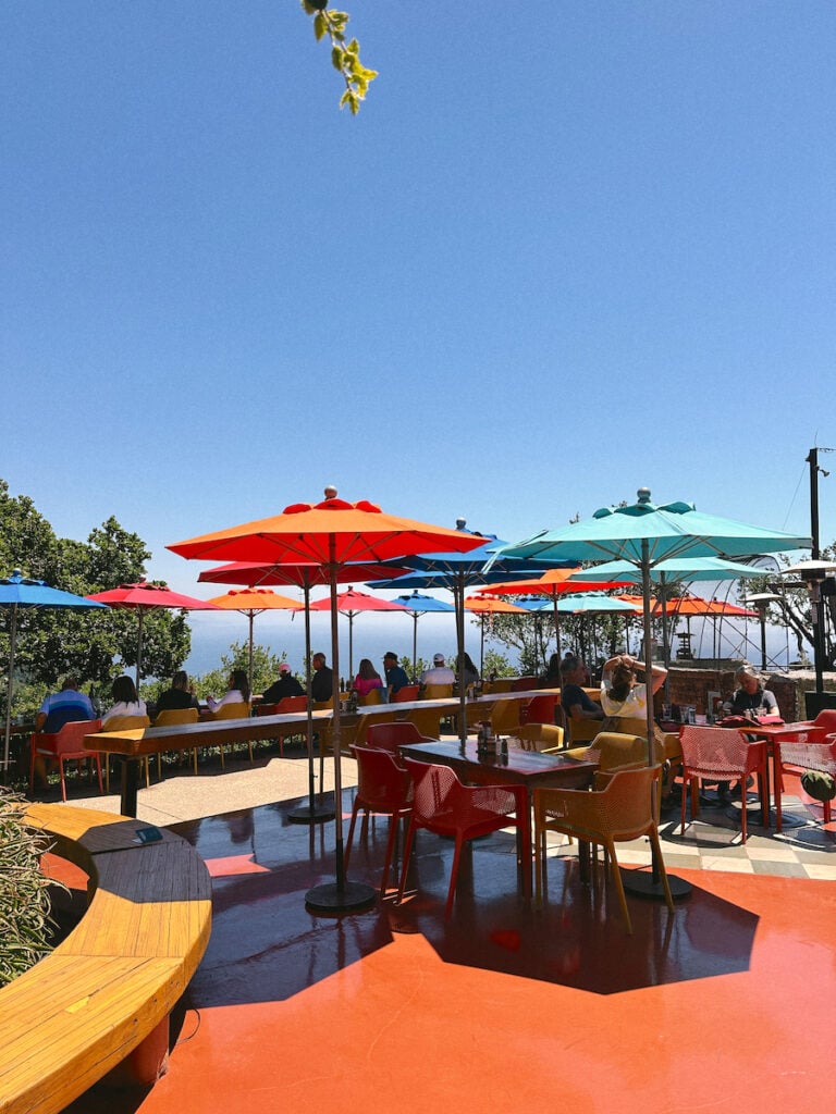 A collection of orange, red, and blue umbrellas above red tables and chairs at the Nepenthe outdoor patio