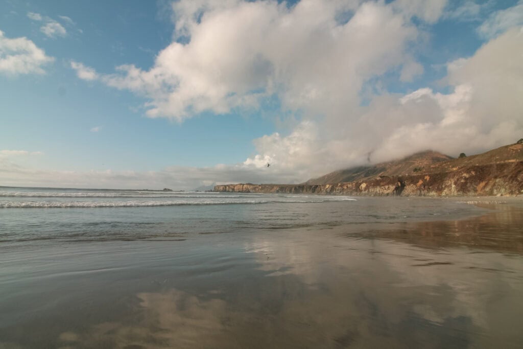 Reflective ocean water on the sand at Sand Dollar Beach. with coastal cliffs in the background