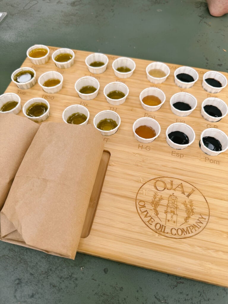 A wooden board with small paper olive oil and balsamic vinegar tasting cups