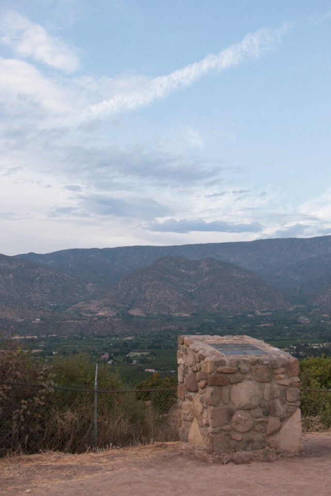 A view overlooking the Ojai Valley and Topa Mountains from the scenic point. There is a stone placard in the foreground. 