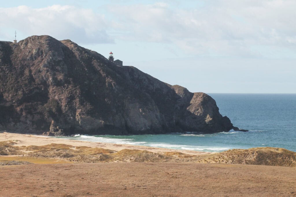 View of the Point Sur Lighthouse on top of a cliff. There is a beach in front of the cliff. 