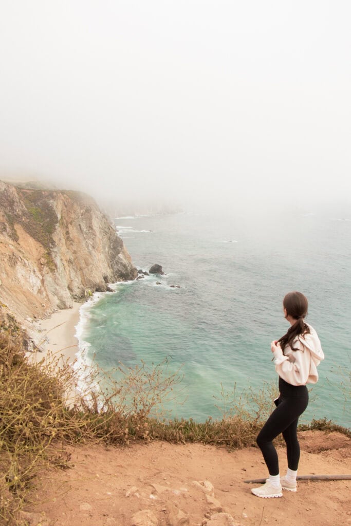 A woman looking out at the Bixby Bridge vista point on a foggy day