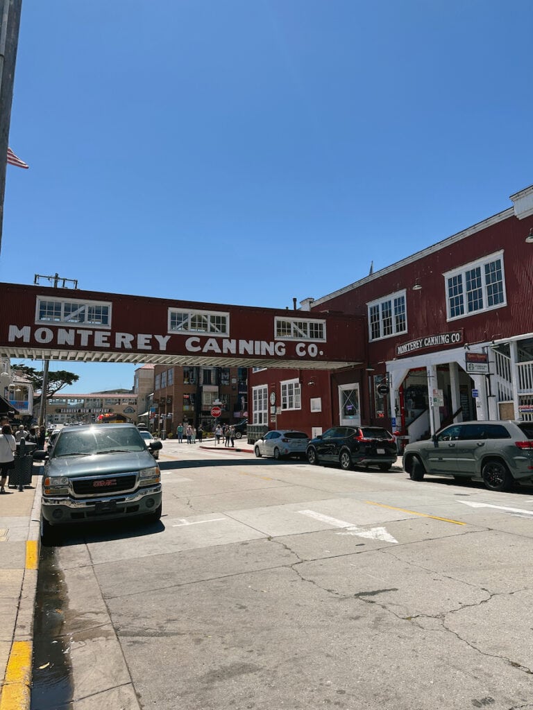 A red building with.a bridge over the road. The bridge has "Monterey Canning Co." written on it.