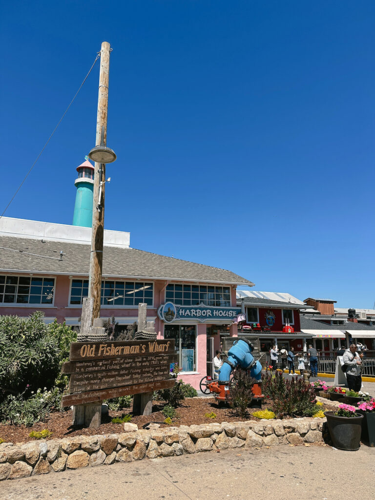 A sign that reads "Old Fisherman's Wharf", with a pink building behind it