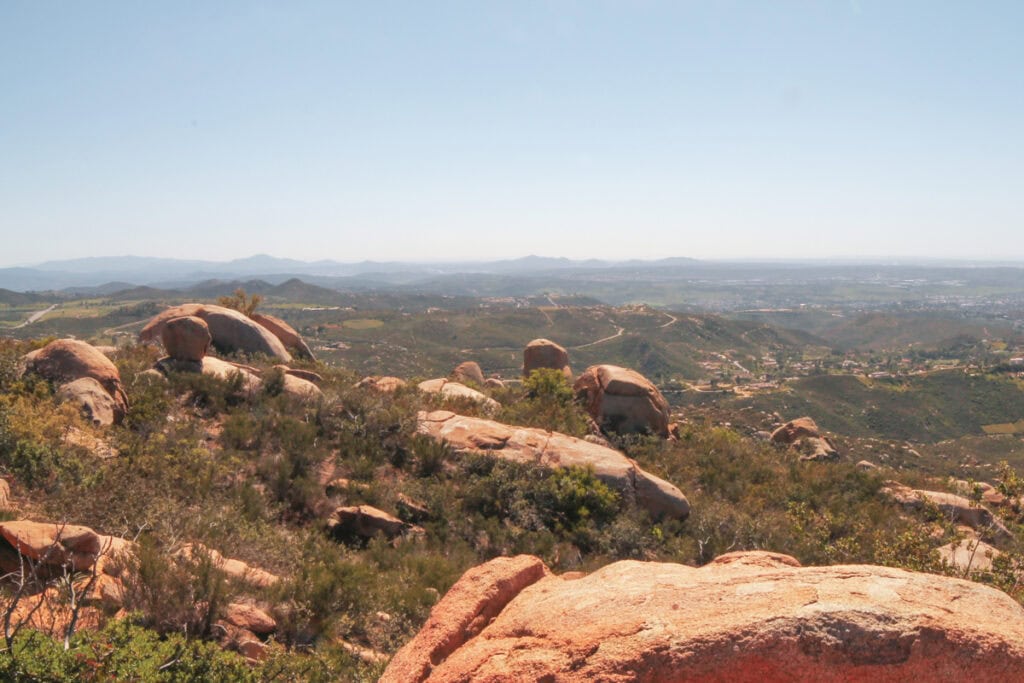 View from the Potato Chip Rock hike of boulders on a mountain and a sweeping vista of the land in the background