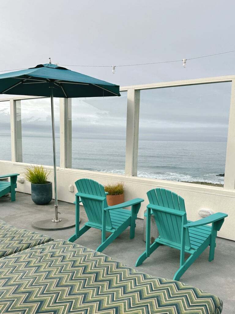 Two teal lounge chairs on a patio looking out at the ocean