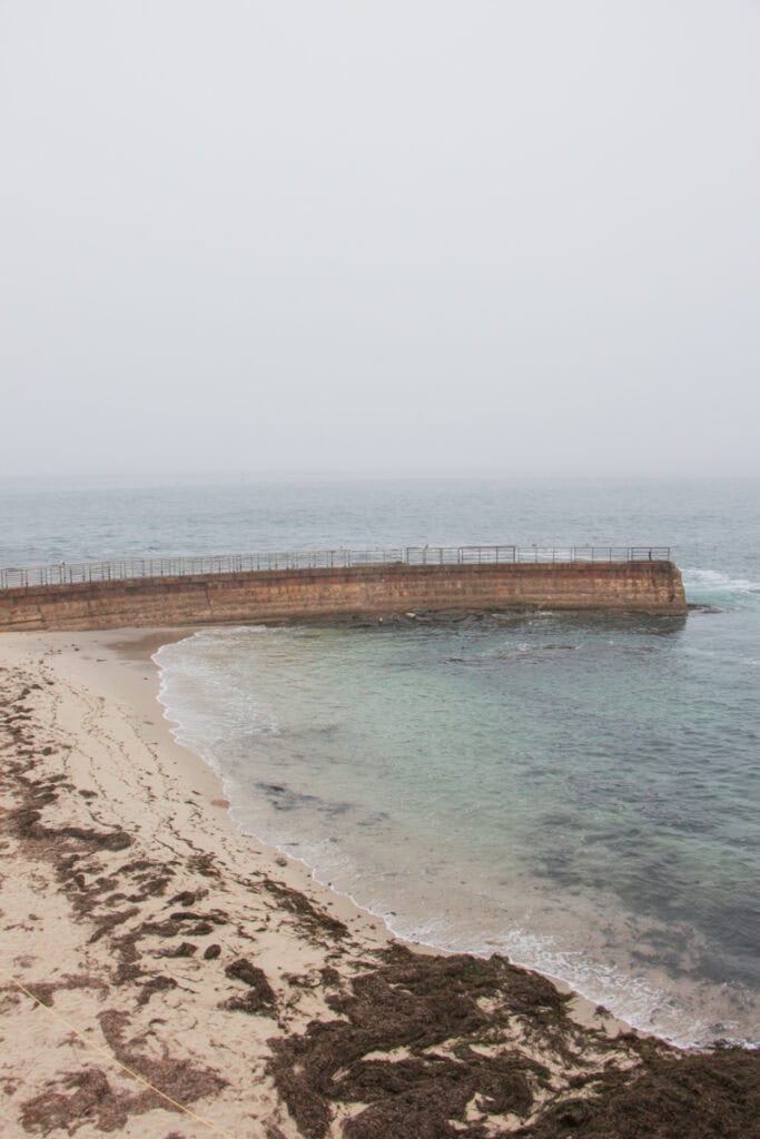 The Children's Pool in La Jolla. There is a sea wall that partially encloses and empty beach. 