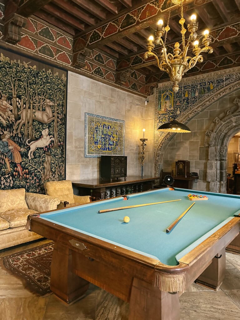 A billiards table in front of a tapestry and intricate tile detailing at Hearst Castle