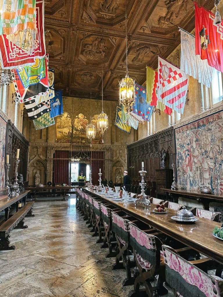 The dining hall at Hearst Castle. There is a long table, and multi-colored flags on either side. 