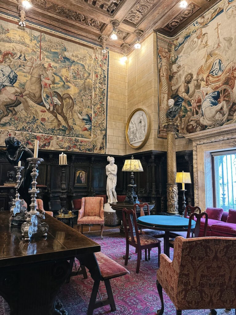 A living space in Hearst Castle filled with artifacts, including a marble sculpture and oversized tapestries on the walls