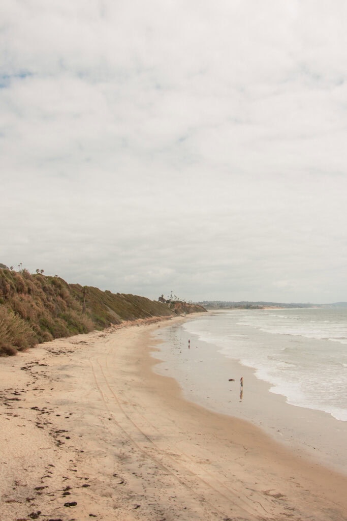 Swami's Beach on a cloudy day. There are a few people walking on the sand.