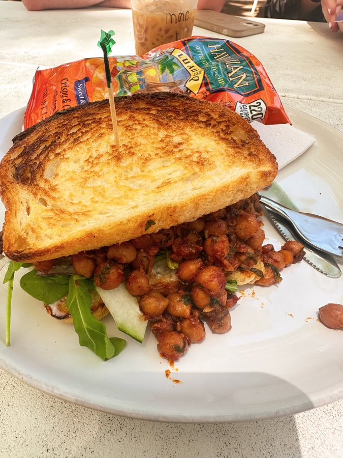A chickpea sandwich on a plate next to a bag of chips