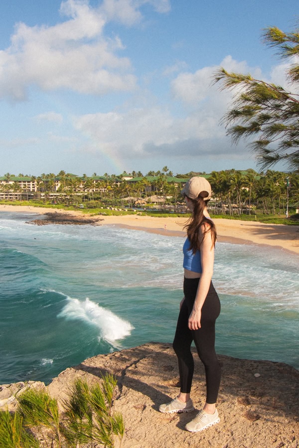 Woman standing on a coastal bluff, looking away from the camera at the ocean and sandy beach