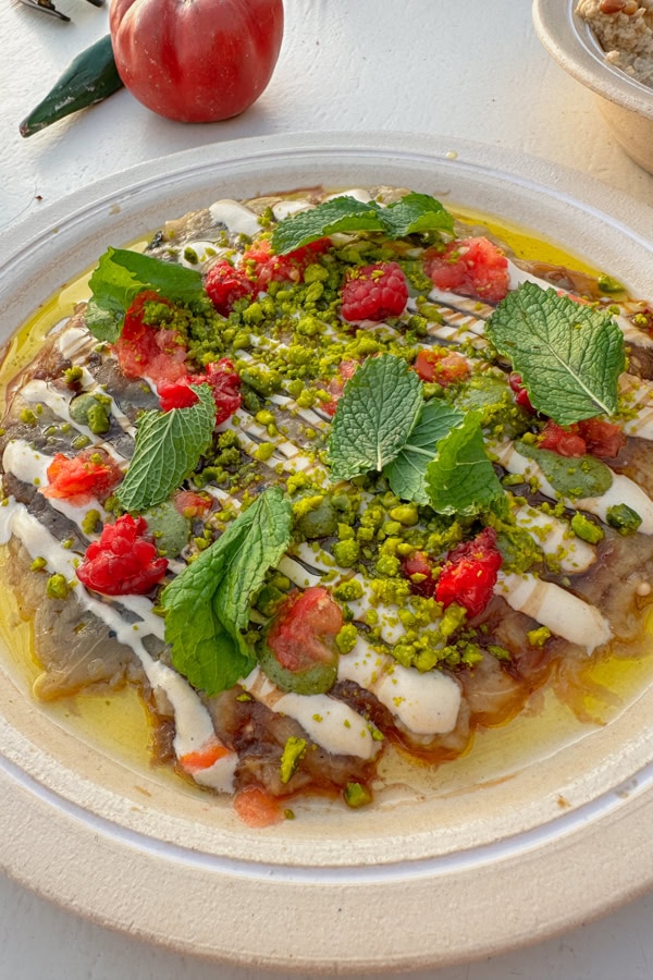 A plate of eggplant covered in raspberries. pistachios, and mint leaves