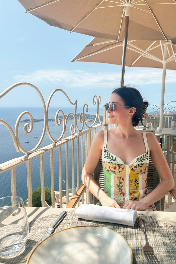 A woman sitting at a patio table looking out at the view of the ocean below