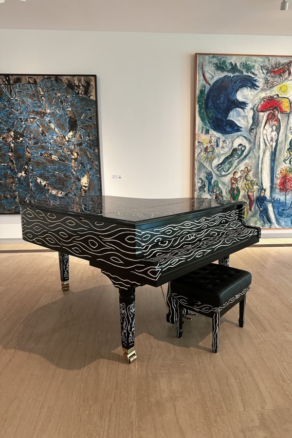 A piano with wave-like detailing on it, and two large paintings behind it