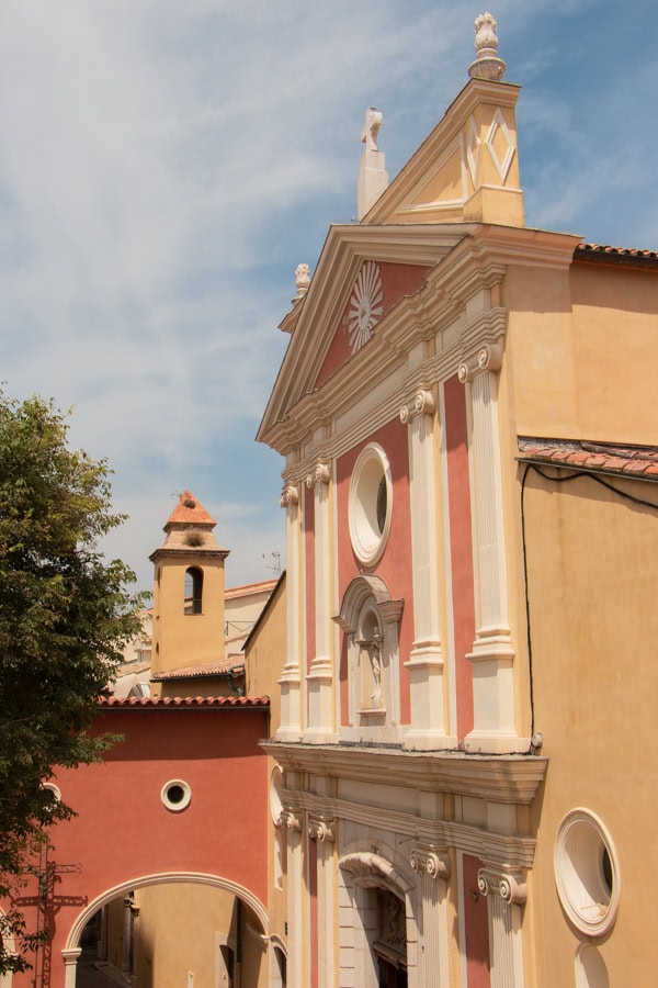 The exterior of a pink, light yellow, and white cathedral in Antibes
