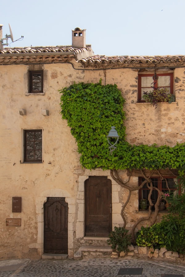 A stone building with two wooden doors and greenery growing up the front