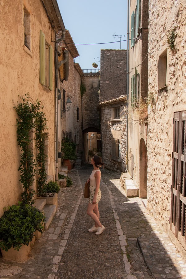 A woman standing in the middle of a narrow passageway, surrounded by stone buildings