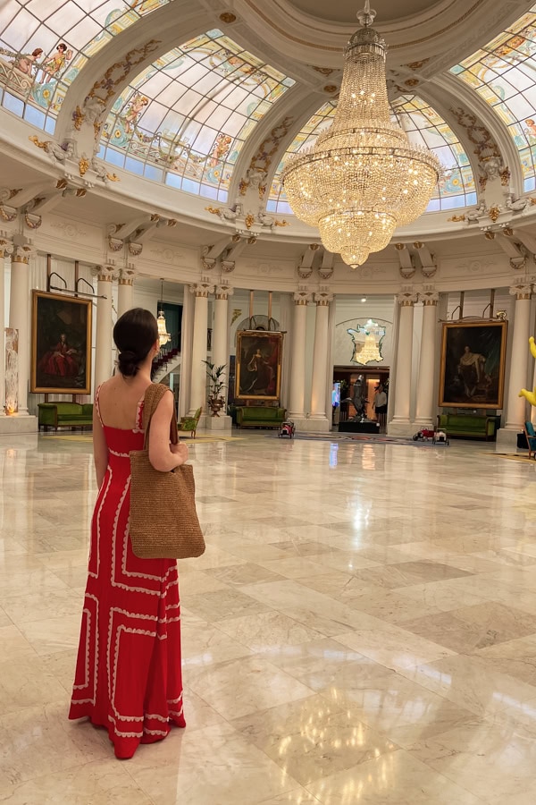 A woman in a red dress looking up at a large, ornate chandelier at the Salon Royal at Le Negresco