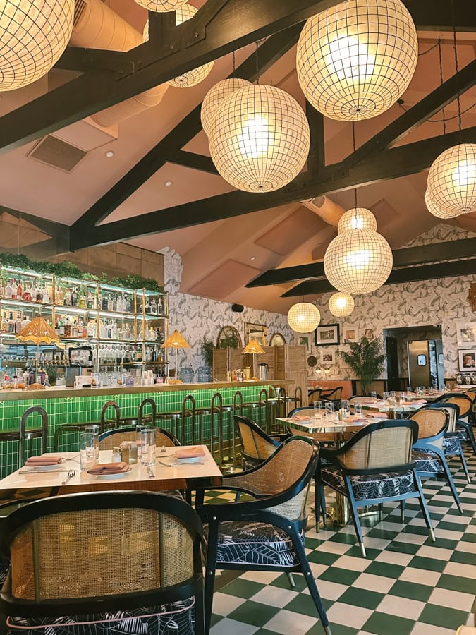 The interior dining room of The Pink Cabana. There is a checkered floor, a green bar, and lanterns hanging from the cieling.