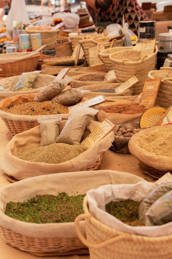 A variety of herbs and spices in baskets on a vendor's table at the Gordes Market