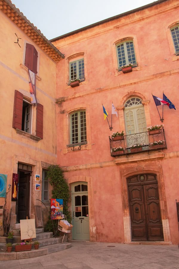A small square in Roussillon with a salmon-colored building next to a pink-tan colored building